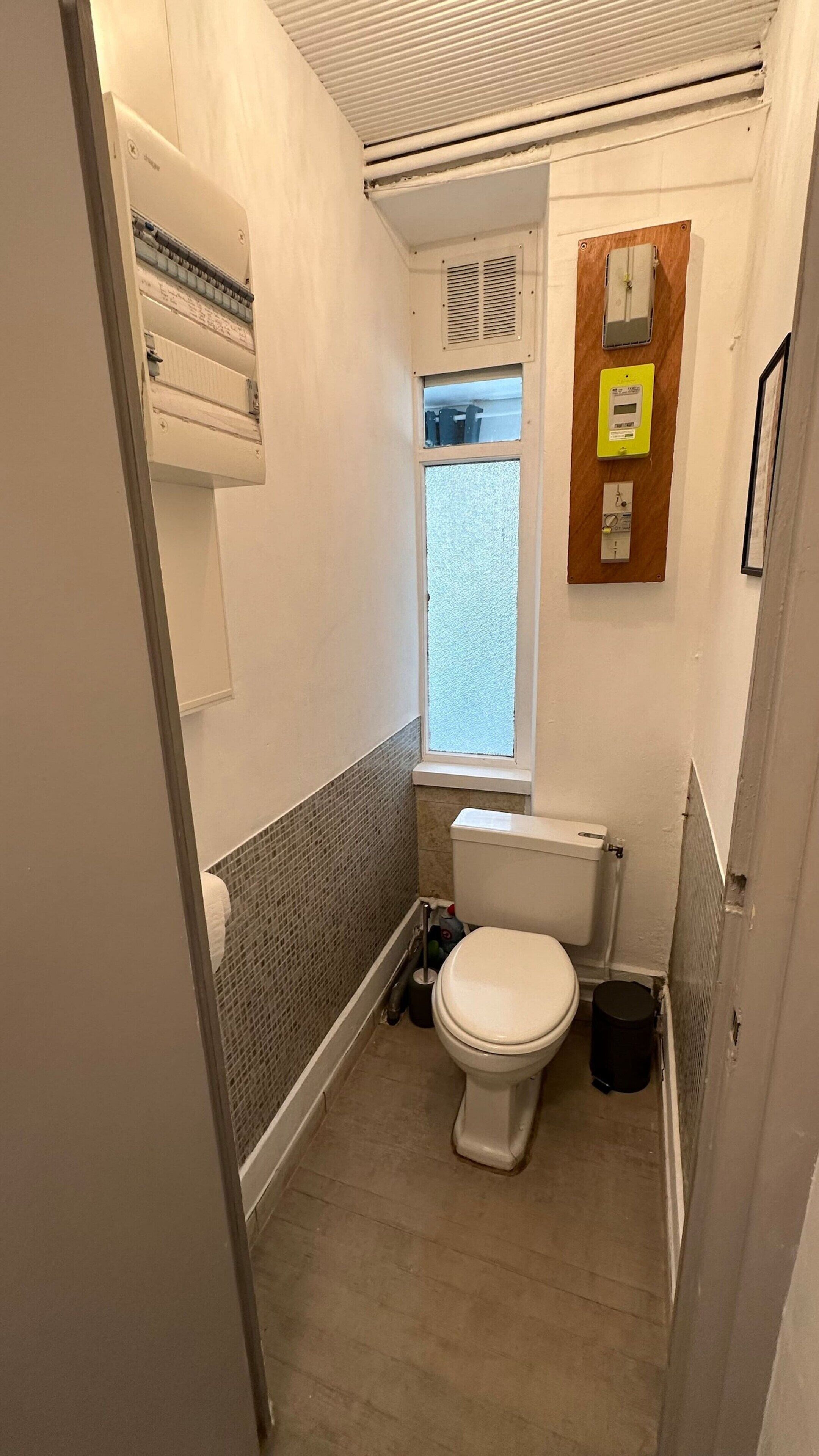 Un baño pequeño y funcional con inodoro, ventana y aire acondicionado de pared.