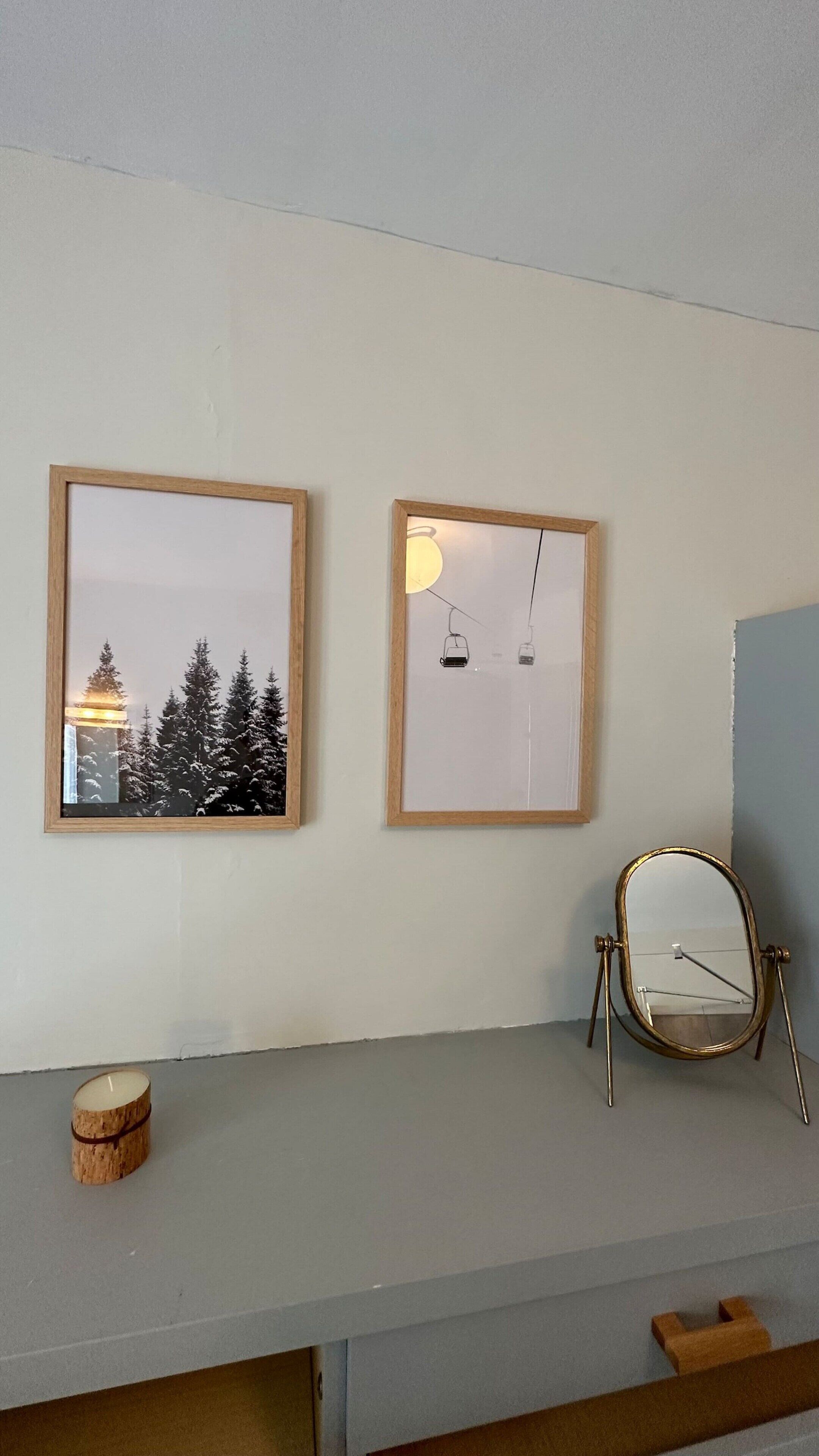 Two framed pictures on a wall, a small round mirror on a stand, and a candle on a table.
