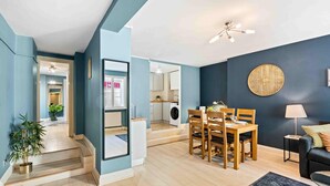 A modern living room with a dining area, a black sofa, and a staircase leading to an upper floor. - Beach Reach | By My Getaways (Brighton)