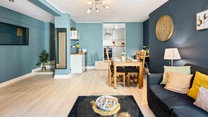 A modern living room with a dark blue wall, a black sofa, and a dining area with a wooden table and chairs. - Beach Reach | By My Getaways (Brighton)