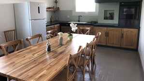 A modern kitchen with wooden cabinets, a dining table with chairs, a refrigerator, and a window providing natural light. - Large, spacious Germaine house in a quiet location 10 minutes from the sea. (Sibiril)