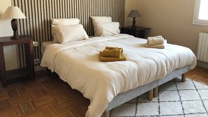 A neatly made bed with white linens and two rolled towels, a bedside table with a lamp, and a wall with vertical stripes and wall art. - Large, spacious Germaine house in a quiet location 10 minutes from the sea. (Sibiril)