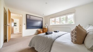 A bedroom with a large bed, a painting on the wall, a window with curtains, and a door leading to another room. - Orchard House 5 bedrooms - sleeps 10 guests  in 5 bedrooms (Burnham Market)