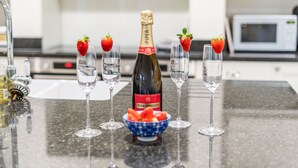 A kitchen counter with a bottle of champagne, a bowl of strawberries, and six glasses. - Orchard House 5 bedrooms - sleeps 10 guests  in 5 bedrooms (Burnham Market)