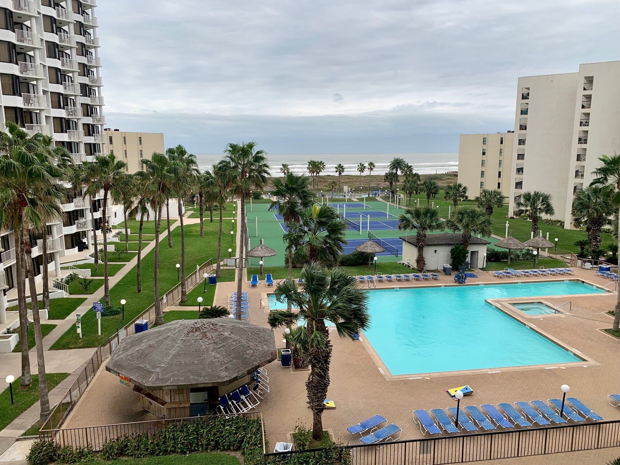 A resort with a swimming pool, tennis courts, and palm trees.