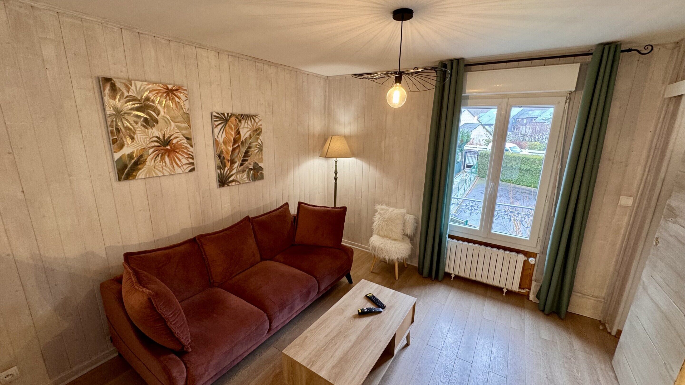 Een woonkamer met een rode bank, een bijzettafeltje, een lamp en twee aan de muur bevestigde schilderijen.