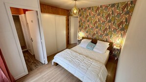 Un dormitorio con una cama, un armario de madera, una puerta y una pared con estampado de hojas tropicales.