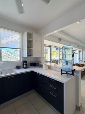 A modern kitchen with a white countertop, black cabinets, a coffee maker, a microwave, and a water dispenser.