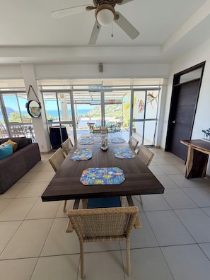 A dining area with a large table, wicker chairs, and a ceiling fan.
