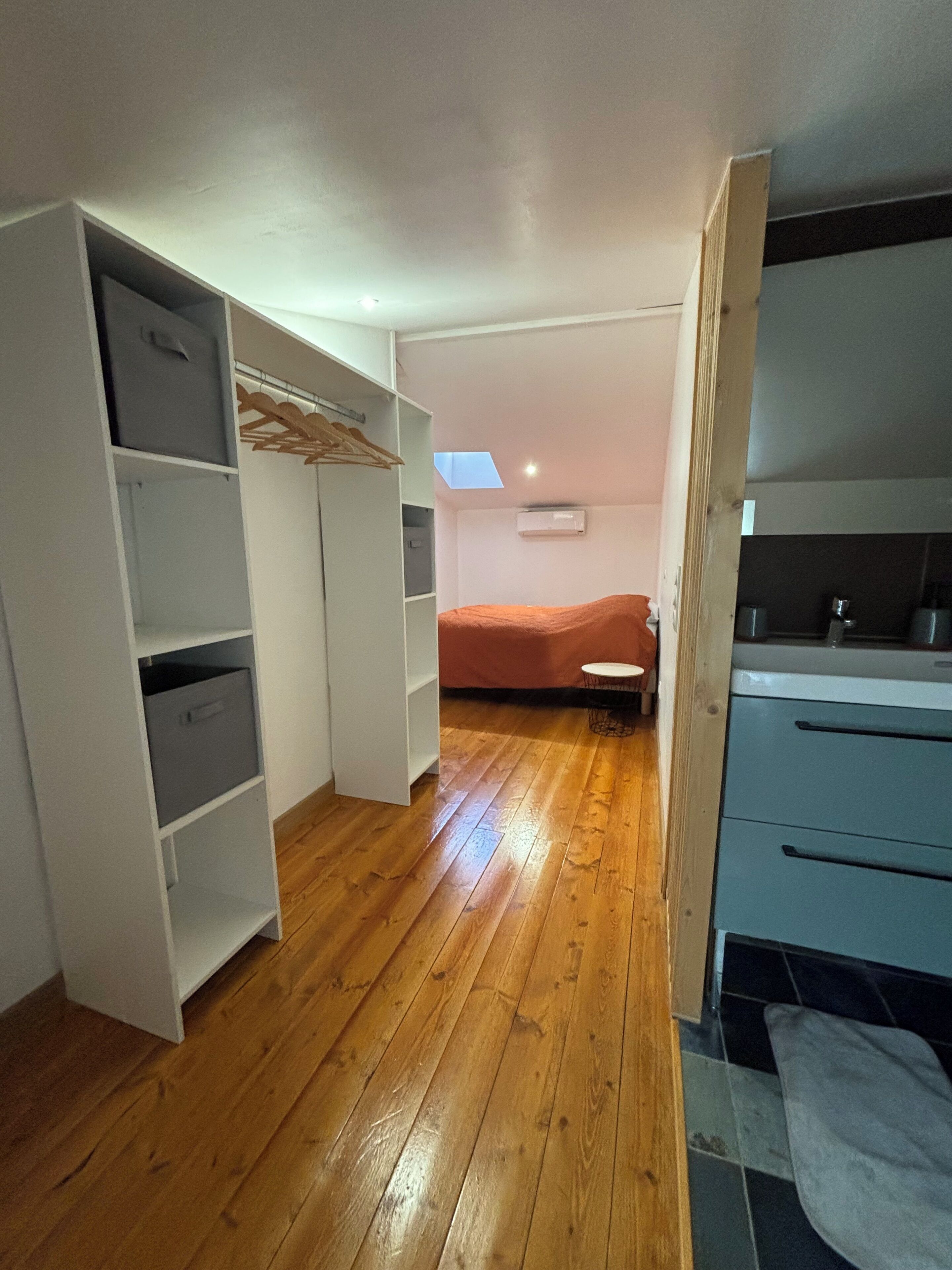 Una habitación con piso de madera, una cama, un armario y una kitchenette.