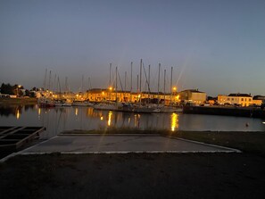 A marina at dusk with boats docked, buildings in the background, and calm water reflecting lights. - Le Chai Poitevin (Marans)