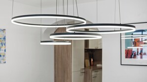 Un comedor moderno con una mesa y sillas blancas, una lámpara de techo circular y un cuadro en la pared.