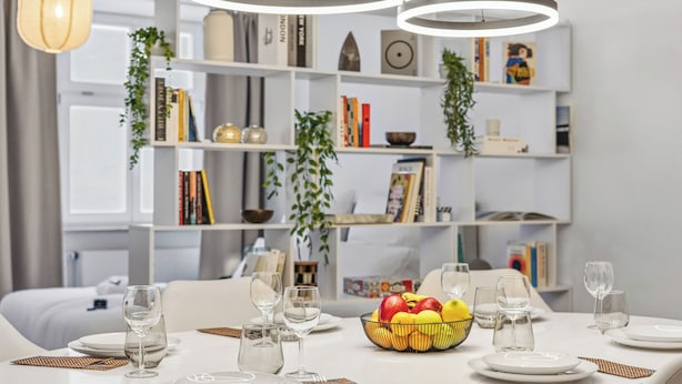 Una mesa de comedor dispuesta con platos blancos, vasos y un frutero.