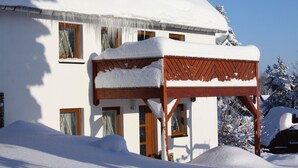 A snow-covered building with a wooden structure on the ground level, multiple windows, and a clear sky. - Haus De Kleene & Gruusse in Mildenau (Mildenau)