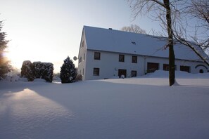 A snow-covered building with a symmetrical facade, a central entrance, and a snow-covered lawn. - Haus De Kleene & Gruusse in Mildenau (Mildenau)