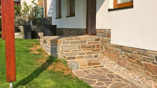 A house with a stone staircase leading to a wooden door, surrounded by a stone wall and a grassy lawn. - Haus De Kleene & Gruusse in Mildenau (Mildenau)
