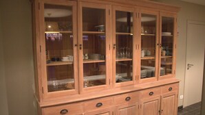 A wooden cabinet with multiple glass doors and drawers, containing kitchenware and dishes. - Countryside Holiday Home (Alveringem)