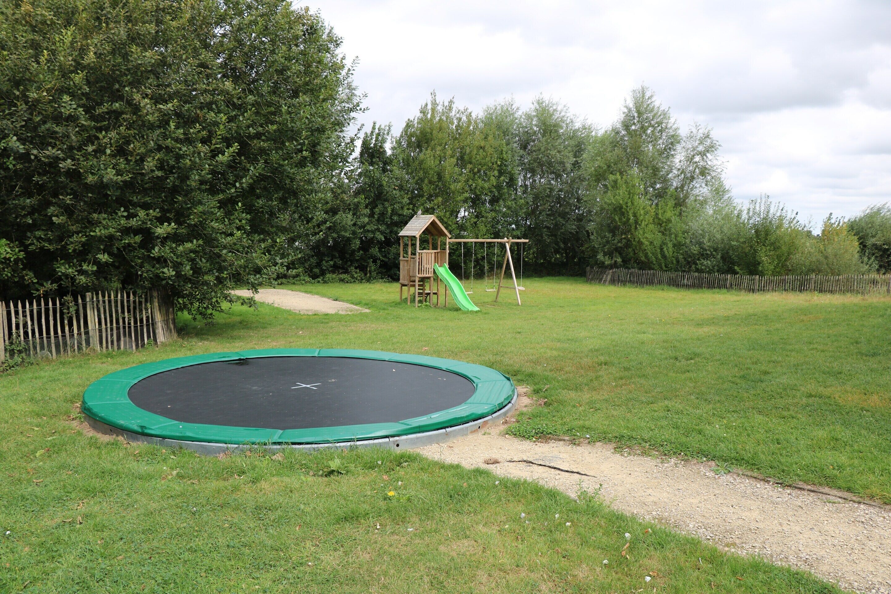 Un parque infantil con un trampolín, columpios y un tobogán.