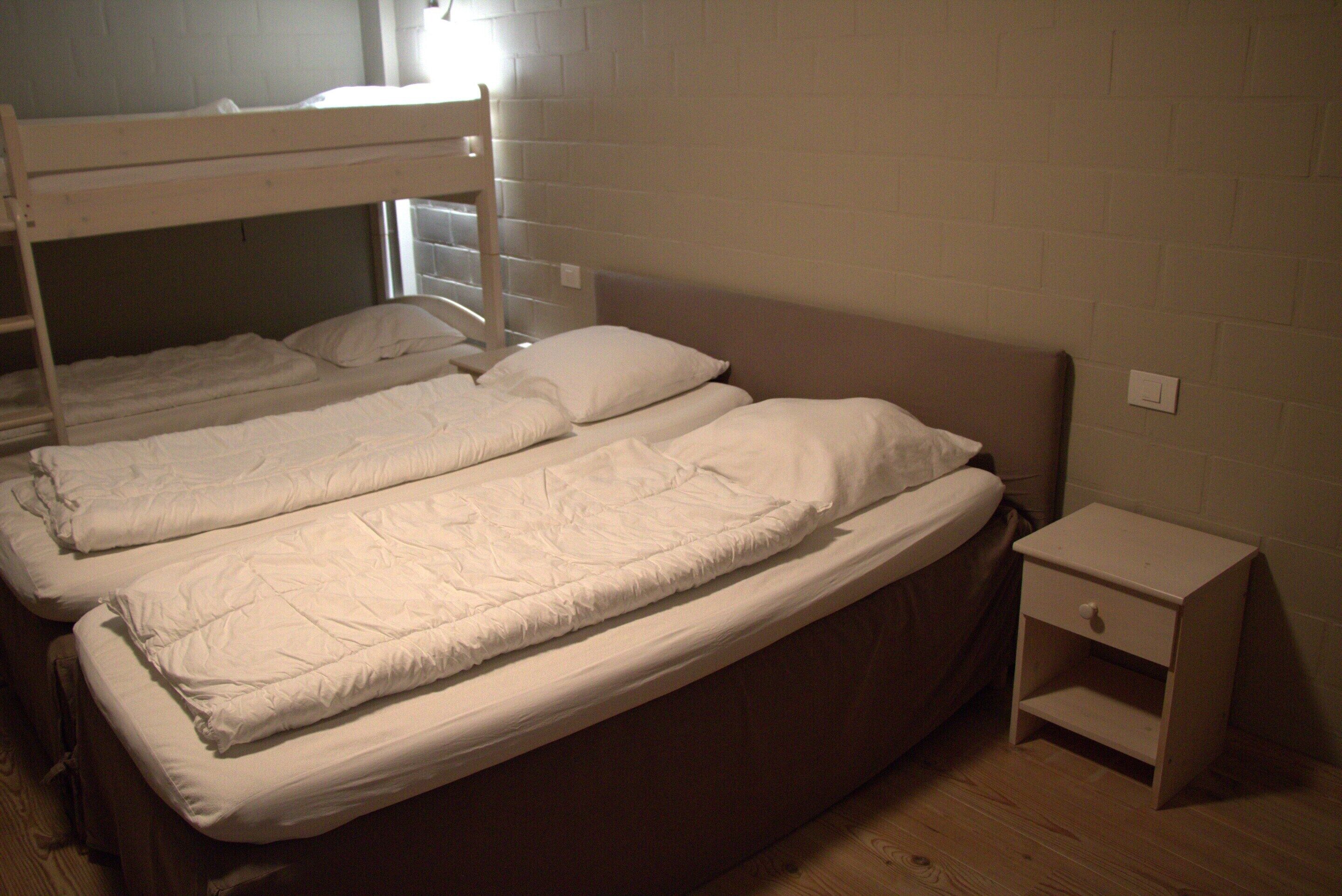 A room with two bunk beds, a small bedside table, and a plain white wall.