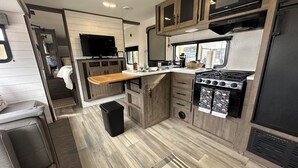 A compact RV kitchen with wooden cabinets, a stove, a microwave, and a TV. - Quiet retreat on beautiful horse farm (Ocala)