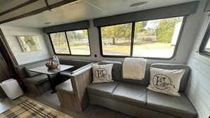 A cozy RV interior with a sofa, a small table, and a window offering a view of the outdoors. - Quiet retreat on beautiful horse farm (Ocala)
