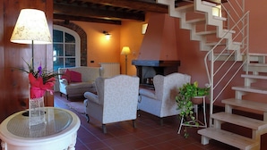 Una sala de estar con chimenea, dos sillones, un sofá, una mesa redonda con lámpara y una escalera.