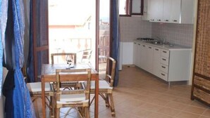Una cocina compacta con gabinetes blancos, un pequeño comedor con una mesa y sillas de madera, y vistas al balcón exterior a través de un ventanal.