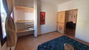 Una habitación con una cama, un armario, una estantería con ropa colgada y una puerta que da a otra habitación.
