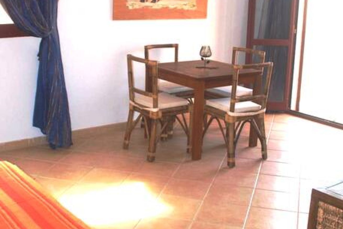 Un área de comedor con una mesa de madera y cuatro sillas, una copa de vino sobre la mesa y una cortina azul a la izquierda.