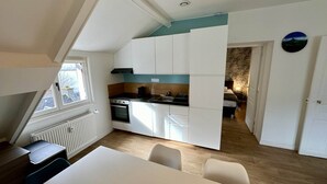 A compact kitchen with white cabinets, a stove, and a dining area with a table and chairs. - Modern Family Villa in La Bourboule (La Bourboule)