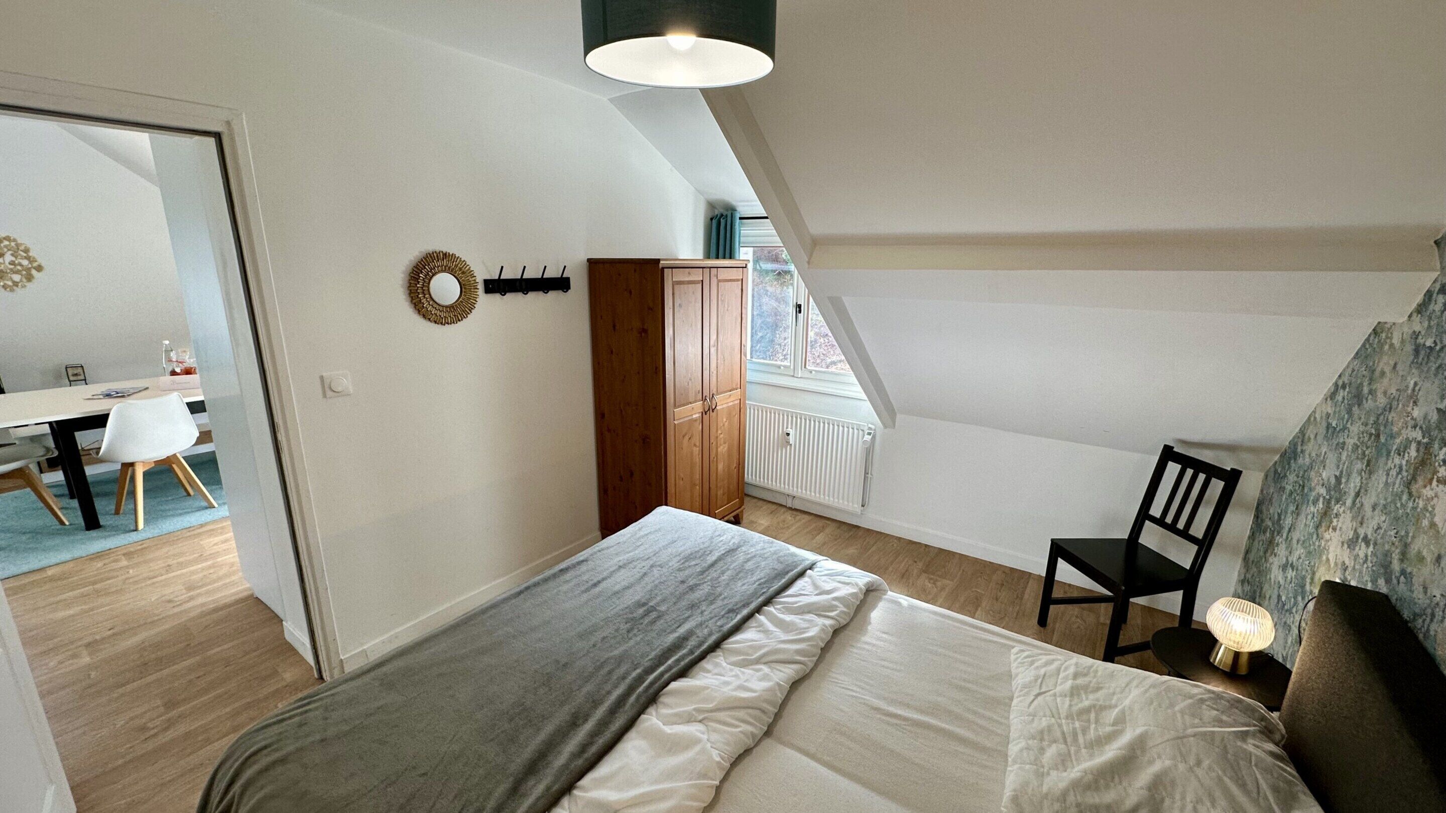 A bedroom with a bed, a chair, a desk, and a wardrobe.