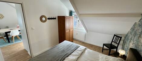 A bedroom with a bed, a chair, a desk, and a wardrobe.