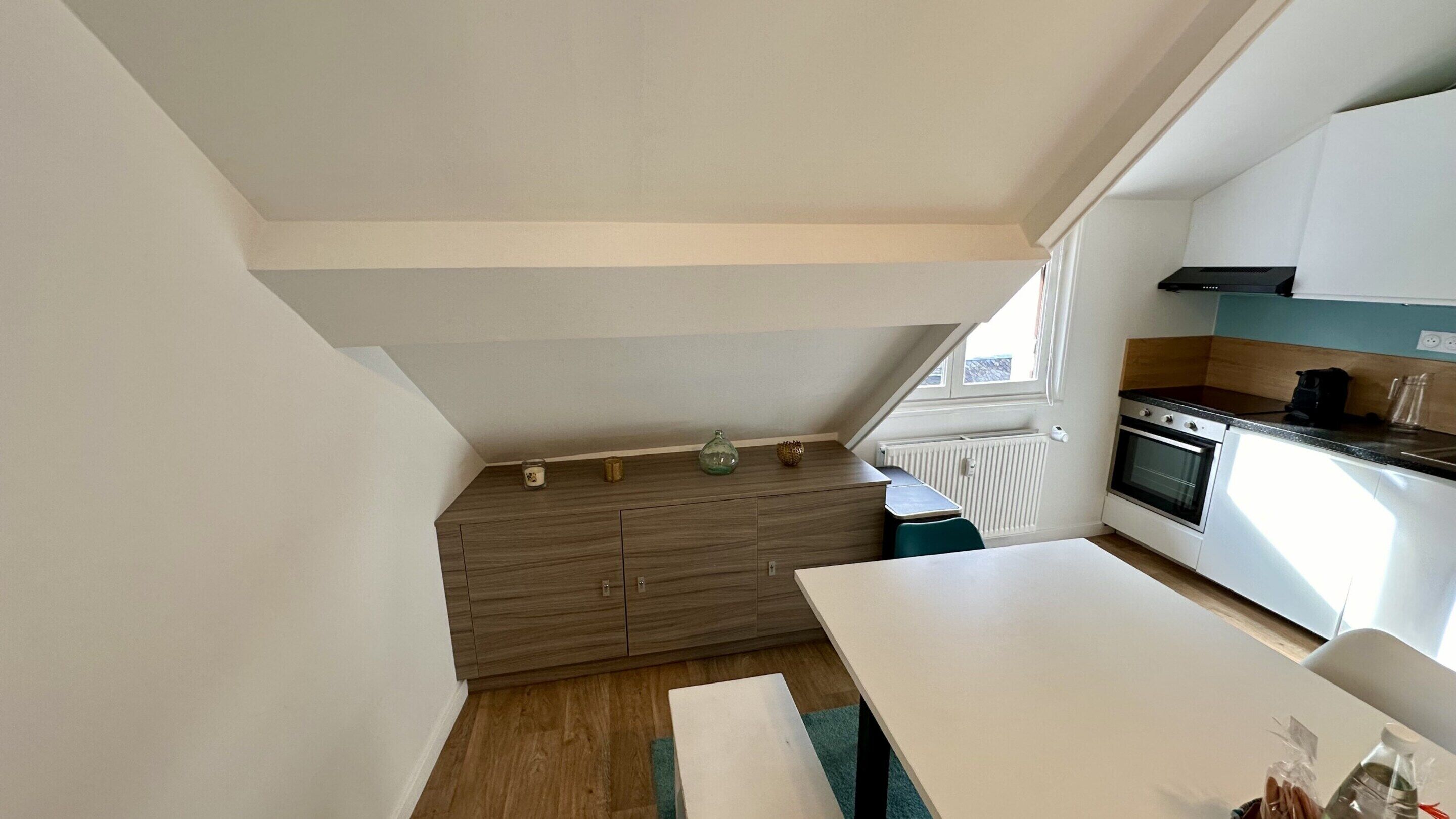 Una cocina compacta con horno integrado, una mesa de comedor y un ventanal que aporta luz natural.