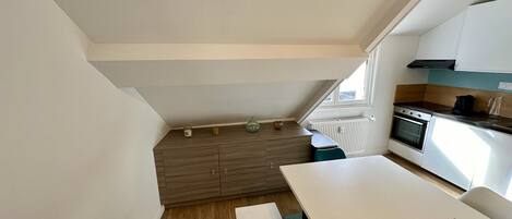 Una cocina compacta con horno integrado, una mesa de comedor y un ventanal que aporta luz natural.