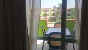 Een balkon met een tafel en stoelen, uitkijkend op een woongebied met groene gebouwen.