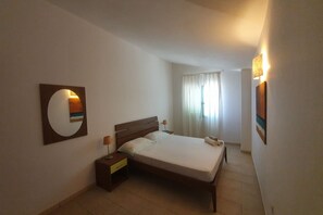 Ein Hotelzimmer mit einem Einzelbett, einem Nachttisch, einer Wandlampe und einem Fenster mit Vorhängen.