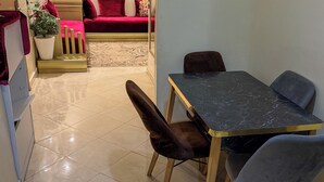 A dining area with a marble table and chairs, a sofa with red cushions, and a potted plant. - 2 balcony rooms in Mabrouka  5 minutes from Guéliz (Marrakech)