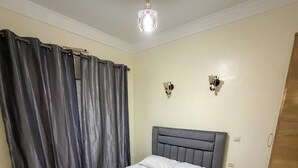 A bedroom with a bed, curtains, a light fixture, and a wall-mounted light. - 2 balcony rooms in Mabrouka  5 minutes from Guéliz (Marrakech)