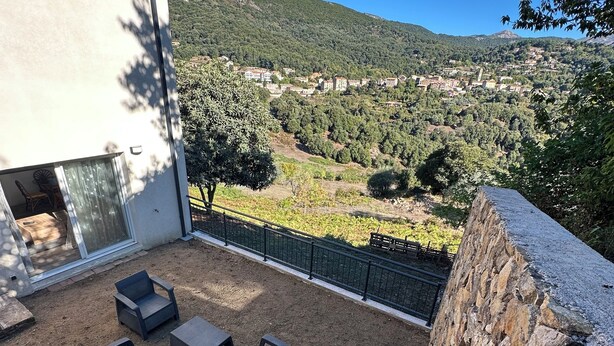 Una terraza con mobiliario exterior, un muro de piedra y vistas a un pueblo y colinas.