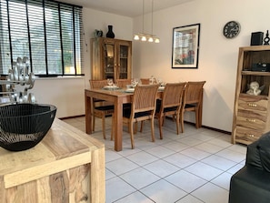 A dining area with a wooden table and chairs, a black woven basket, and a cabinet with glass doors. - Modern Holiday Home With Garden (Sint Maartensvlotbrug)