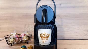 Une machine à café Nespresso, accompagnée d’une tasse et de trois gobelets à café, le tout posé sur une surface en bois.