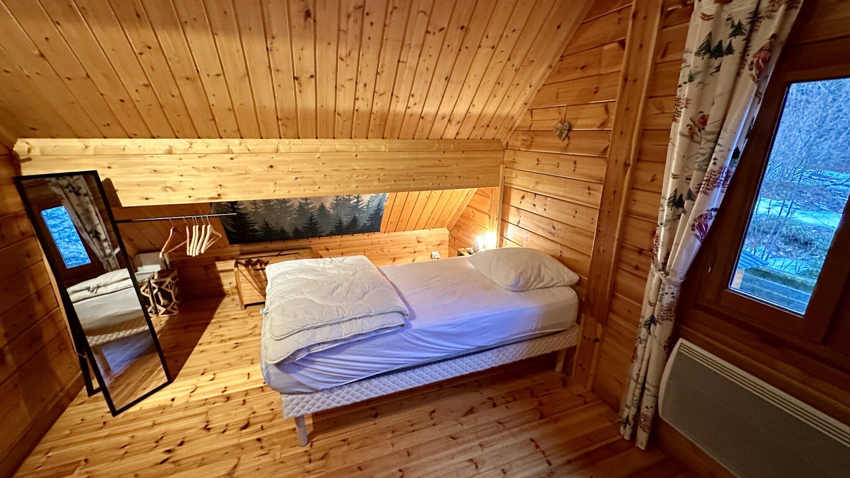 Quarto acolhedor de cabana de madeira, com cama, espelho e janela com cortinas.