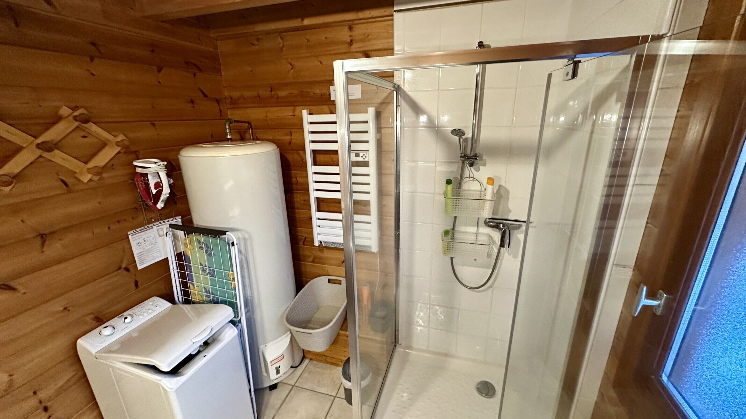 A compact bathroom with a glass-enclosed shower, a white washing machine, and a large water heater.