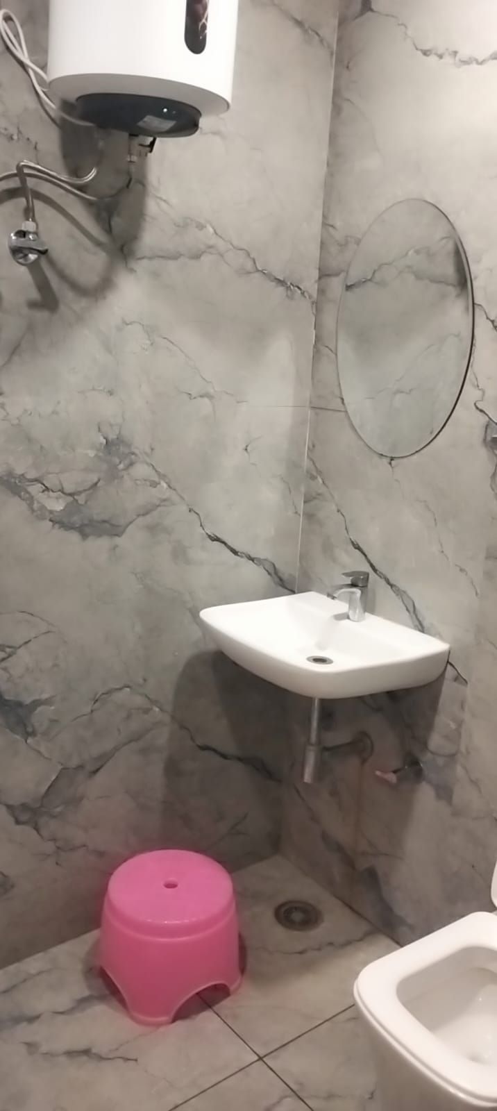 A bathroom with a marble wall, a white sink, a pink stool, and a toilet.