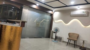 A reception area with a glass door, a reception desk, a standing fan, and a chair. - The Garrison Hotel (Meerut)