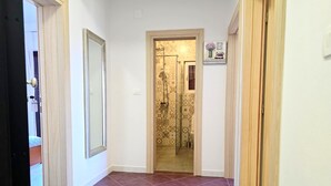 A hallway with a tiled floor leading to a bathroom with patterned tiles and a shower. - Apartment Gina in Zaton (Nin)