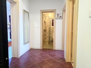 Un couloir doté d’un sol carrelé qui mène à une salle de bain aux carreaux décoratifs et équipée d’une douche.