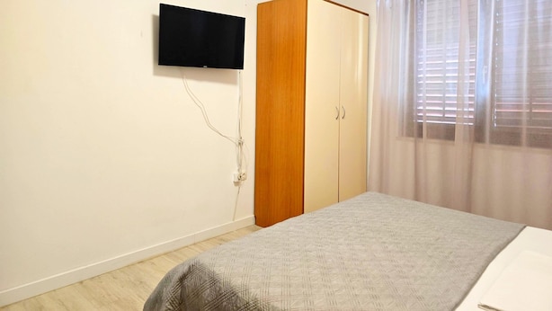 A bedroom with a bed, a wardrobe, a television mounted on the wall, and a window with curtains. - Apartment Gina in Zaton (Nin)