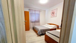 A bedroom with two beds, a wooden door, a window with curtains, and a painting on the wall. - Apartment Gina in Zaton (Nin)