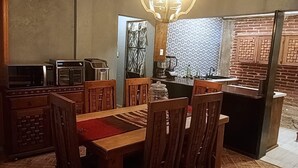 Un coin repas avec une table et des chaises en bois, un coin cuisine équipé d’une machine à café et un mur en briques.